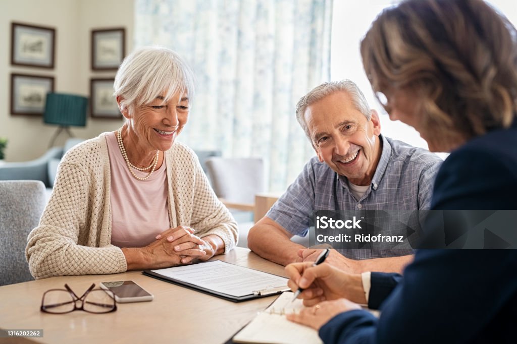 Senior couple planning their investments with financial advisor at home. Happy aged couple planning their medical insurance with advisor in living room. Old couple consulting with insurance agent while sitting together at home.